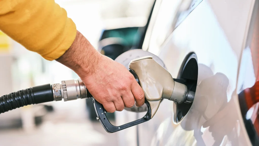 Close-up of a person wearing a yellow long-sleeve shirt holding a fuel nozzle inserted into the gas tank of a white car